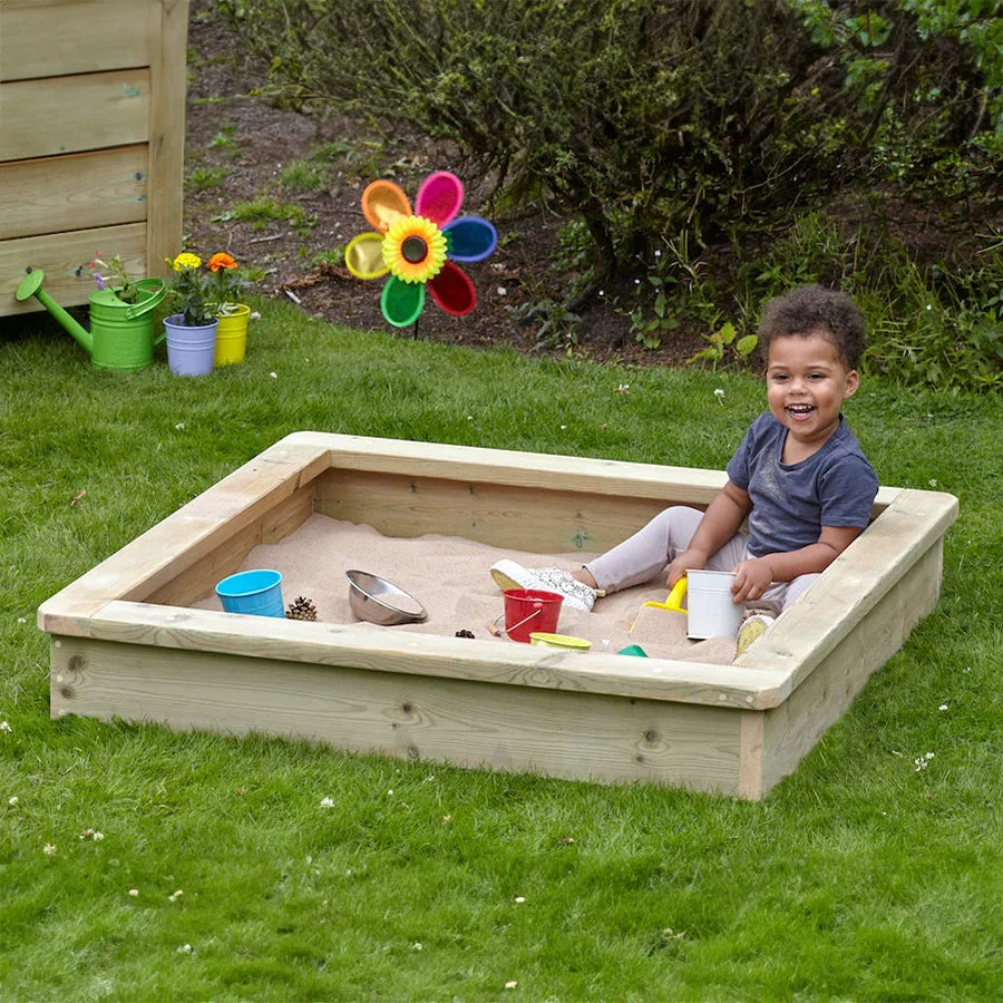 Child playing in a sandbox with toys on a grassy area