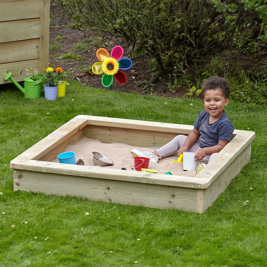 Child playing in a sandbox with toys on a grassy area